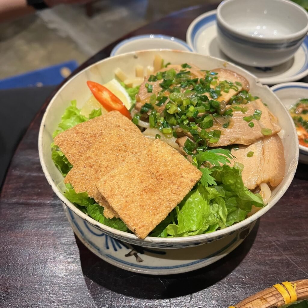 A bowl of cao lau noodles with pork, herbs and crispy rice crackers in Hoi An